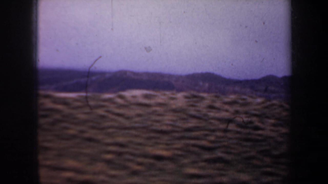 Rolling scrubby hills and distant ridge under a pale purple sky.