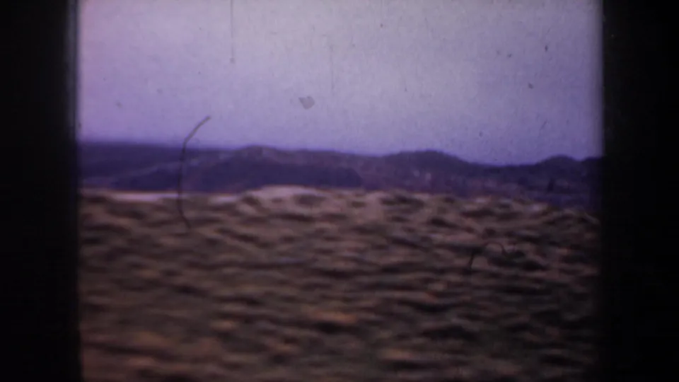 1957 Oregon countryside frame showing rounded scrub hills, a distant dark ridge, and a pale sky with visible 8mm film wear.