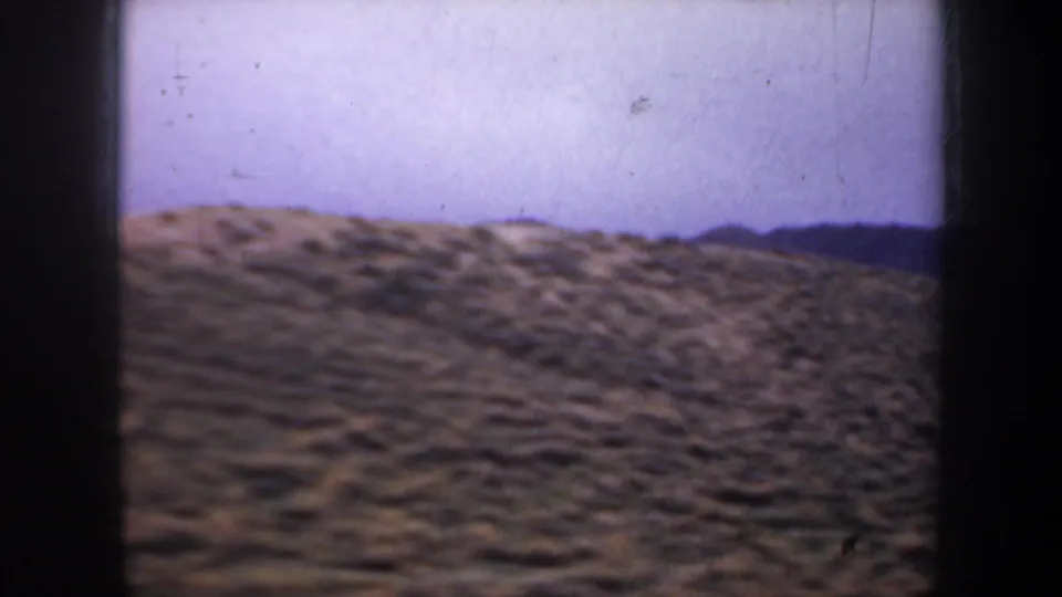 1957 8mm frame of open Oregon hill country with scrub-covered slopes, distant ridge line, and soft purplish film color.