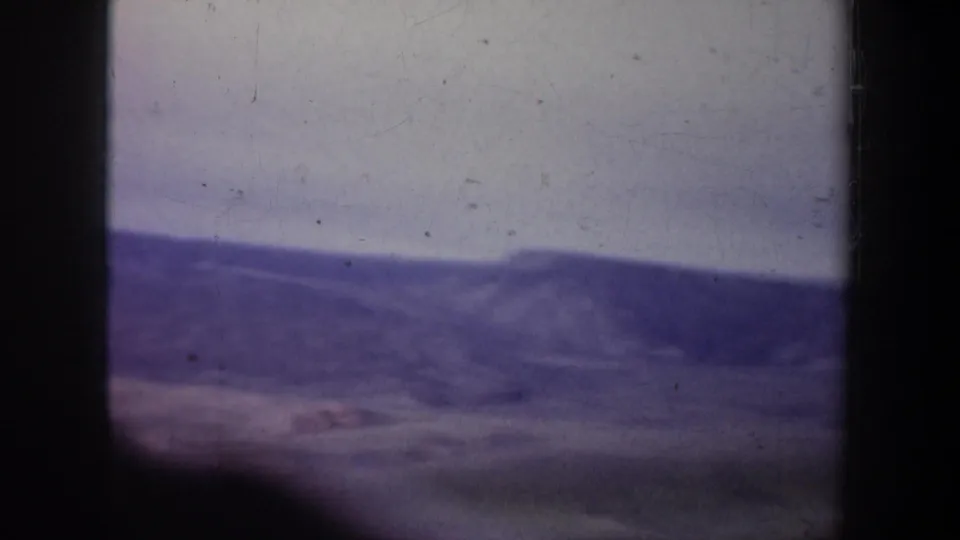 Wide 1957 Oregon home-movie view of rolling hills and distant low ridges, softened by grain, haze, and purple-tinted color.