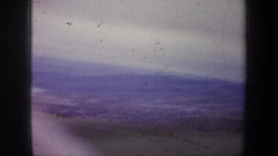 Purple-tinted 8mm frame from the Portland, Oregon landscape clip, with distant hills, open land, and an overcast sky.