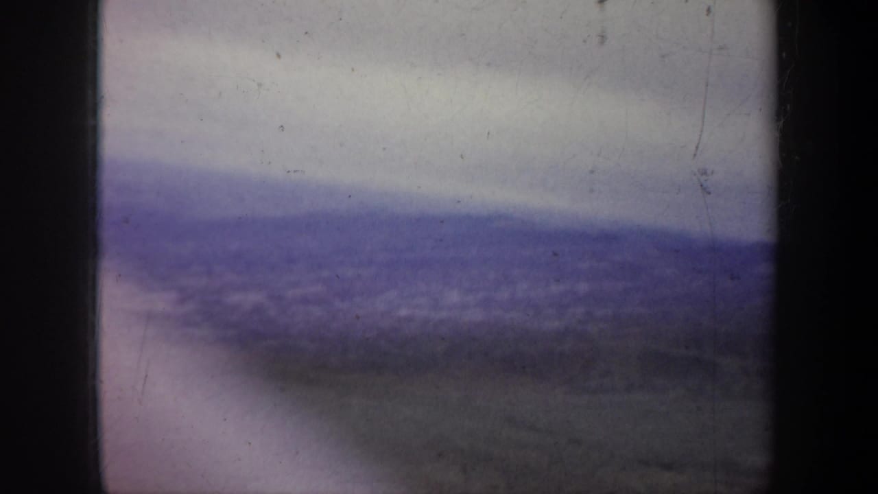 1957 home-movie frame from the Portland, Oregon metadata showing a soft, hazy mountain view through an airplane window.
