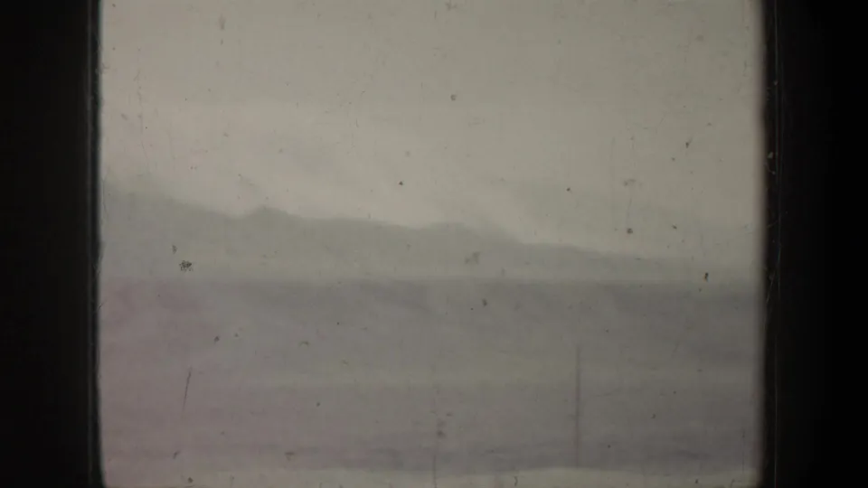 Hazy 1957 airplane-window view with a distant mountain ridge, pale sky, and dark vertical frame edge.