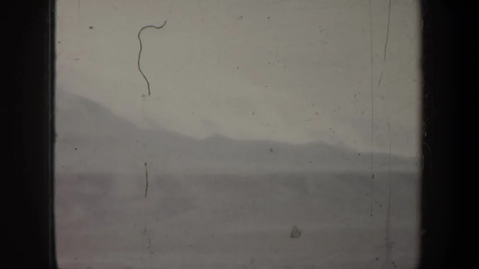A soft 1957 Portland-region travel frame shows distant mountains through a dark aircraft window with visible dust and scratches.