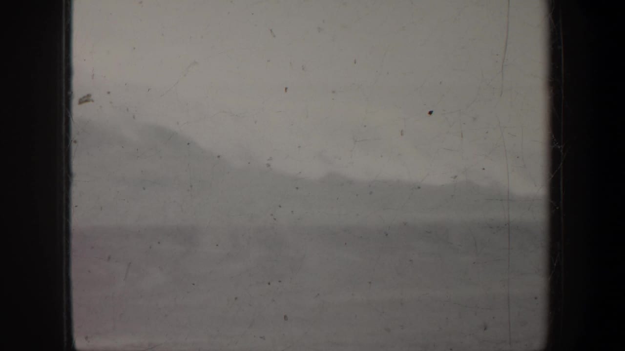 1957 Oregon 8mm frame showing a soft, foggy mountain ridge with dark film gate edges and visible dust marks.