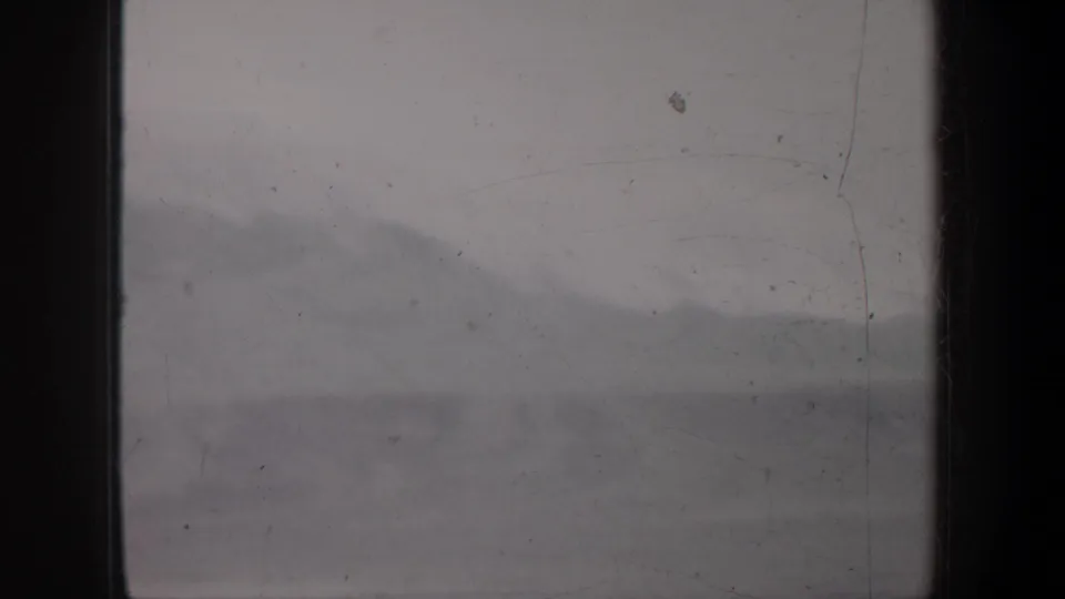 1957 Oregon home-movie frame with a hazy mountain silhouette, pale snow patches, and prominent dark vertical film borders.