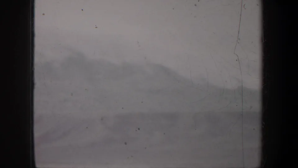 1957 Oregon 8mm view of a low snowy mountain slope, softened by haze, dust, scratches, and dark gate edges.