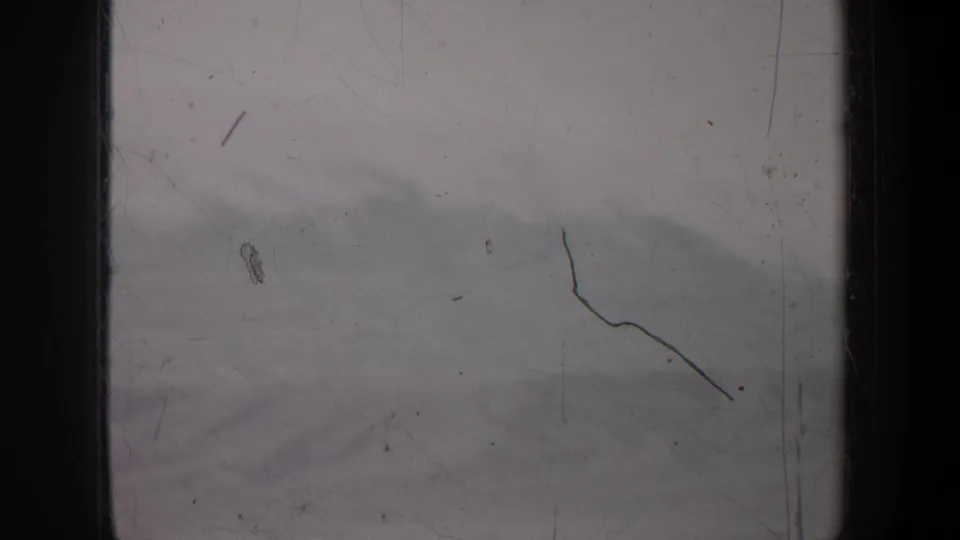 1957 Oregon home-movie frame showing a soft snow-covered mountain slope with visible scratches, dust, and black gate edges.