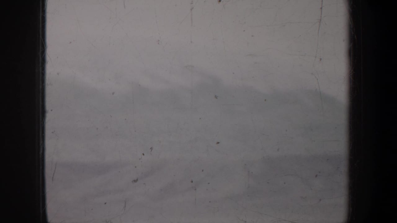 1957 Portland, Oregon metadata frame showing a dim, scratched 8mm view of a pale haze and indistinct distant landform.