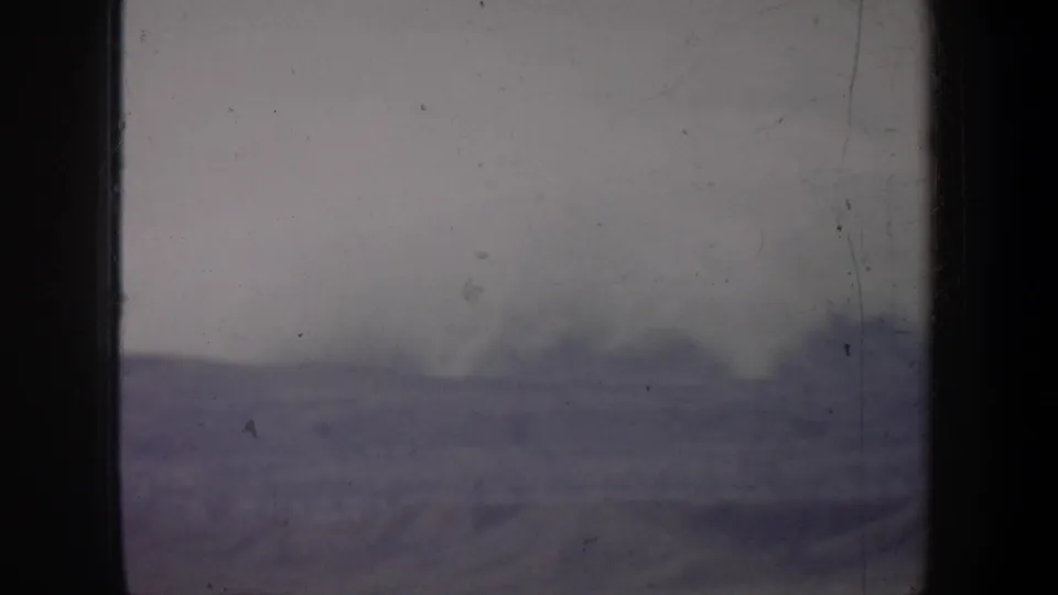 1957 8mm footage metadata shows a washed, scratched view of a low barren-looking horizon under a pale, foggy sky.