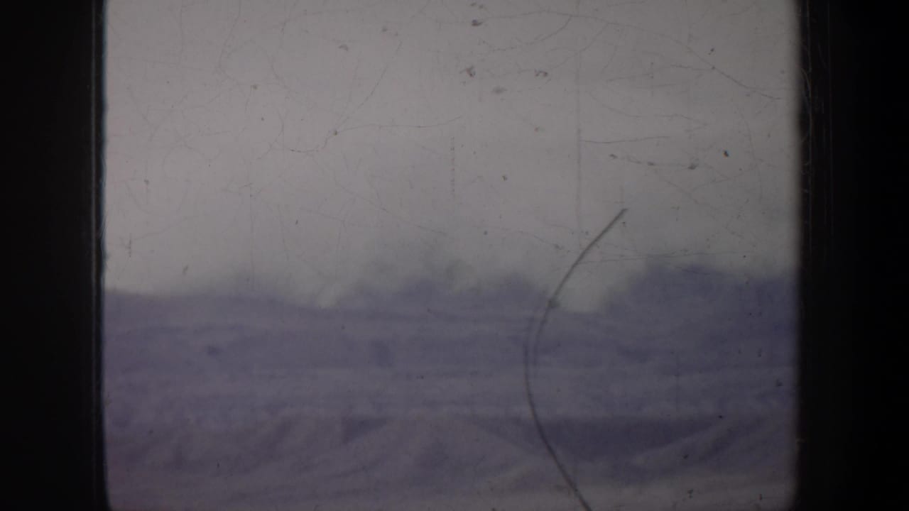 1957 Oregon 8mm frame showing a faint snow-covered mountain landscape through scratches, dust, and soft exposure.