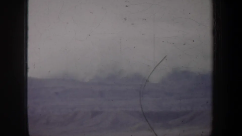 1957 Oregon 8mm frame showing a faint snow-covered mountain landscape through scratches, dust, and soft exposure.