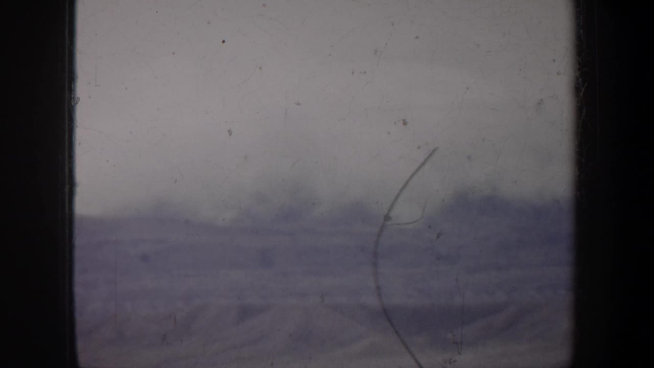 1957 Oregon home-movie frame with a blurred snow-covered ridge line, muted color, and visible 8mm film damage.