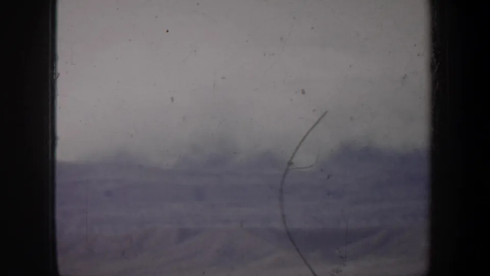 1957 Oregon home-movie frame with a blurred snow-covered ridge line, muted color, and visible 8mm film damage.