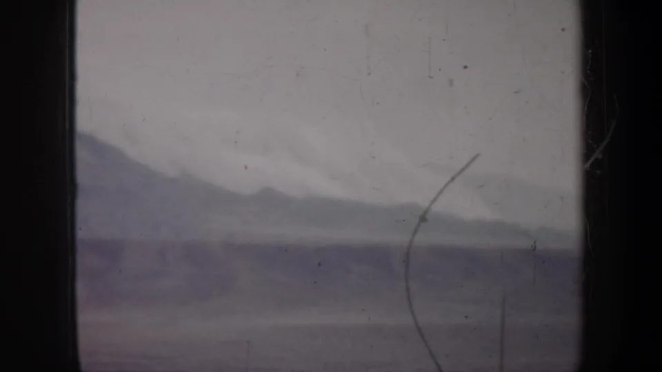 1957 Oregon 8mm frame showing a soft mountain slope and snowfield under overcast light, with visible scratches and dust.