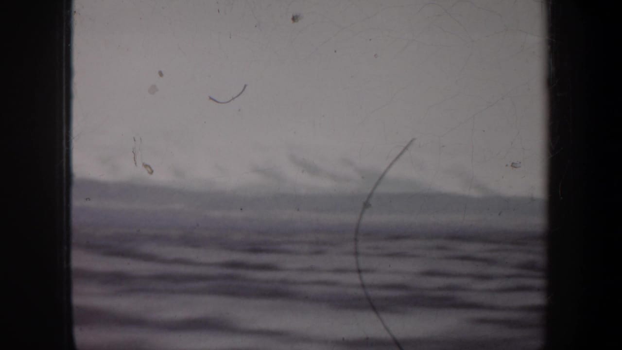 1957 8mm home-movie frame showing a soft ocean horizon and low waves through dark vertical framing.