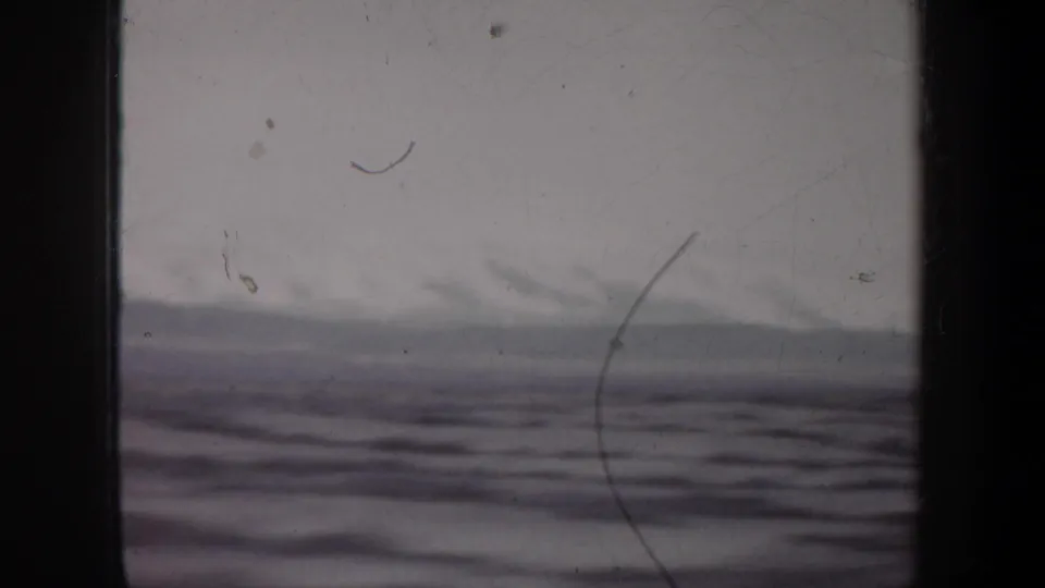 1957 8mm home-movie frame showing a soft ocean horizon and low waves through dark vertical framing.