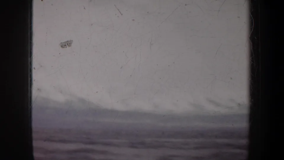 1957 home-movie frame with a pale sky, blurred waterline, dark framing, and visible film wear.