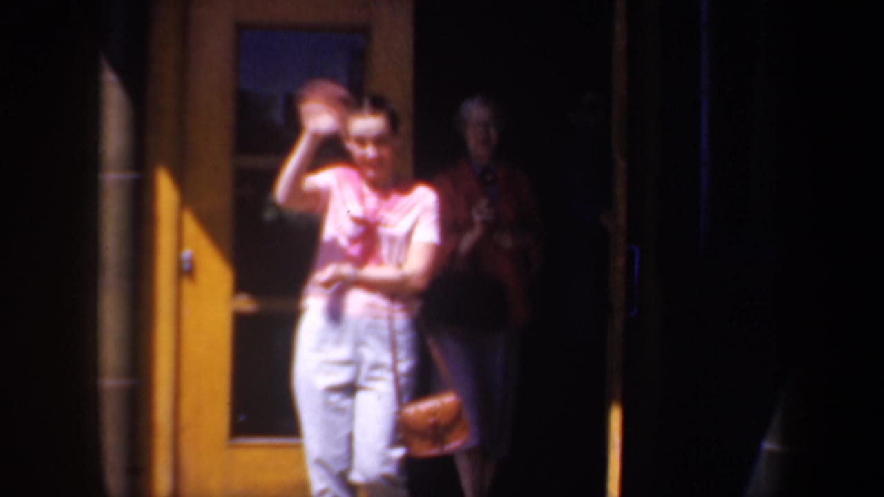In 1957 Portland home-movie footage, a young woman in a pink top waves from a doorway with another figure behind her.