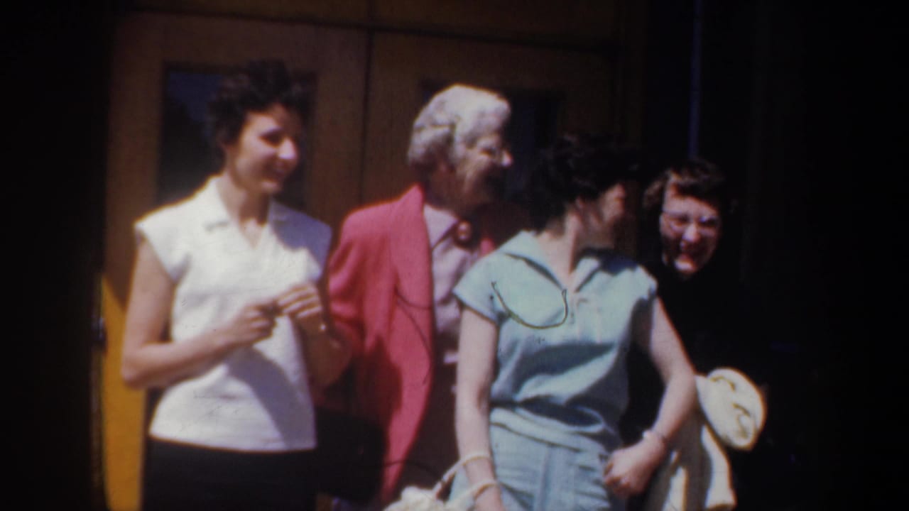 Four women in 1950s clothing stand outside a building in Portland, Oregon, smiling and conversing in bright sunlight.