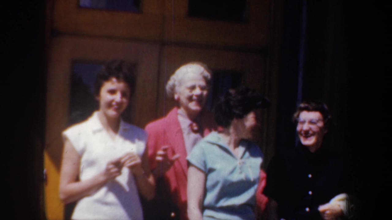 A 1957 home-movie frame shows four women outside a building in Portland, with faces visible and period clothing in sunlight.