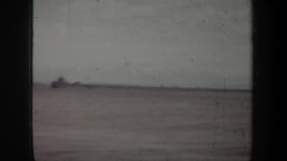 Blurred 8mm frame showing an indistinct open landscape or water view with a low horizon and small dark form at left.