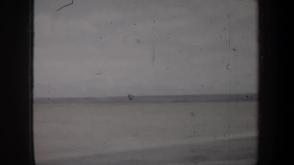 Archival 8mm view from a moving road trip, showing a low horizon and pale sky with visible film wear and gate edges.
