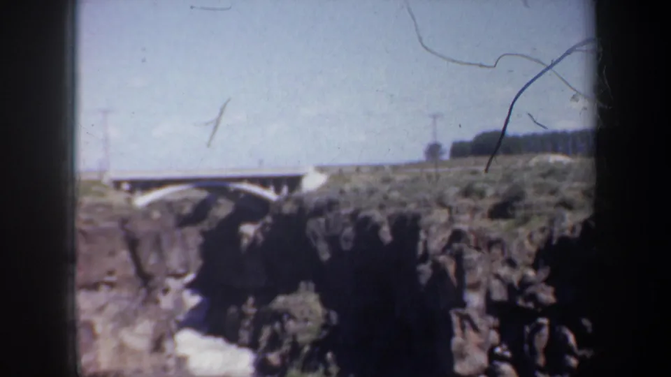 1957 8mm frame of the Oregon bridge and canyon, with scratches and soft focus visible across the home-movie image.