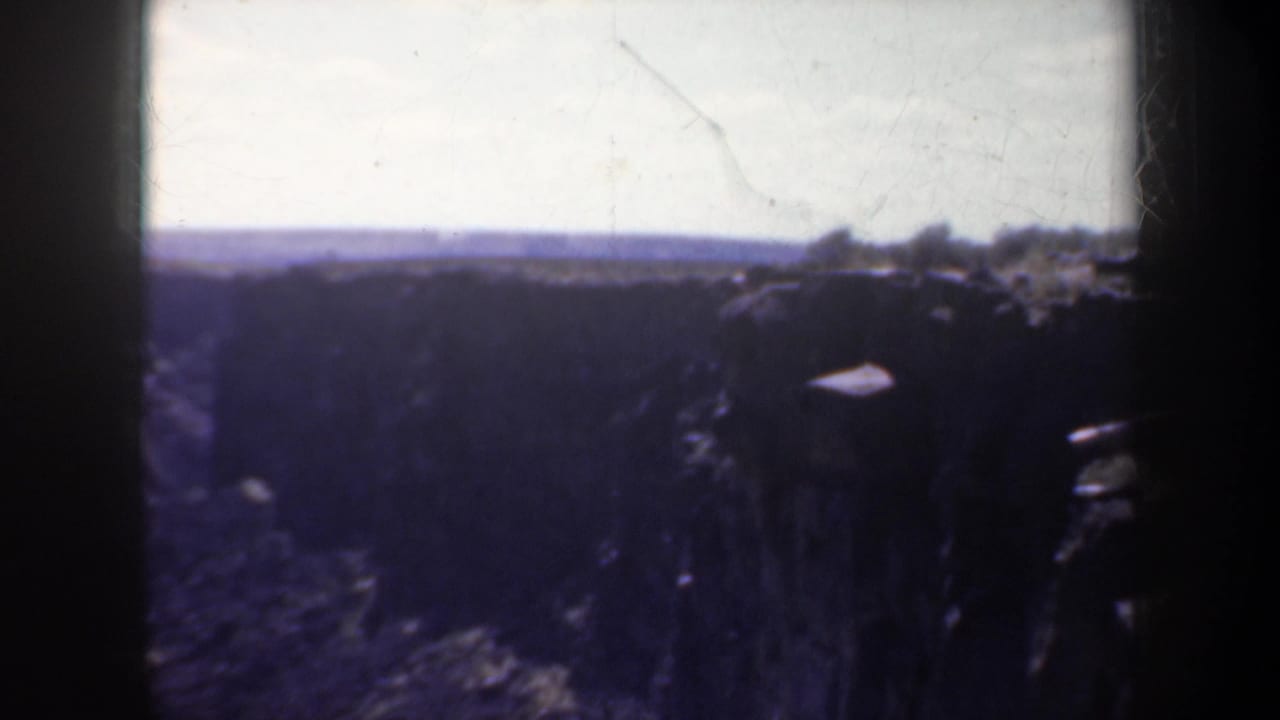 1957 Oregon 8mm frame showing a dim, wide canyon view with rocky cliffs and a pale horizon.