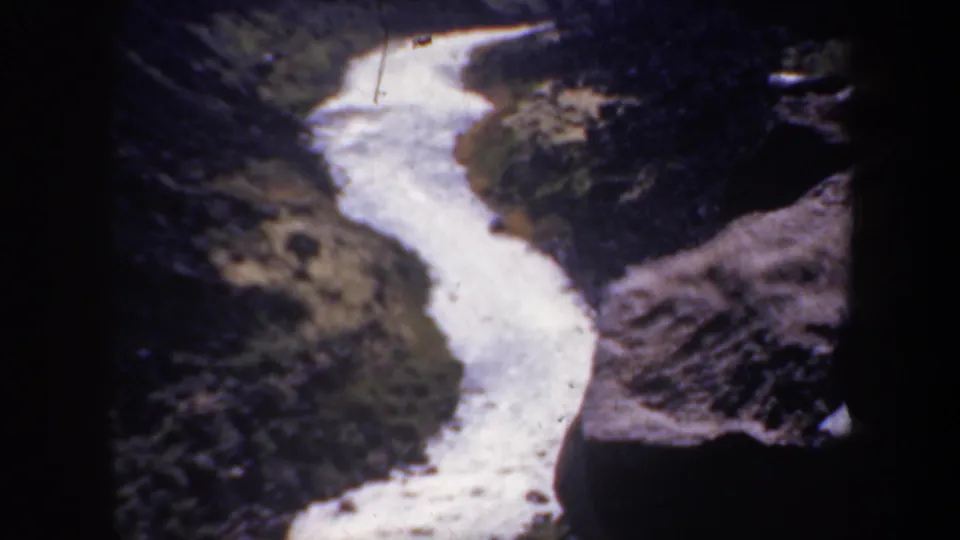 1957 Oregon 8mm frame focused on a bright meandering river between rugged canyon slopes.