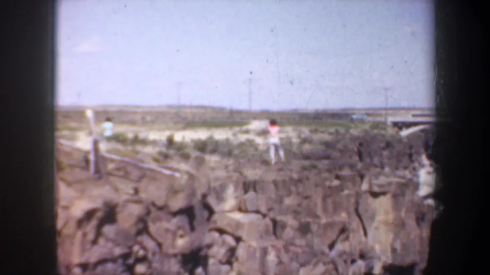 A 1957 Oregon overlook view shows distant visitors near a fenced canyon rim above rocky cliffs.