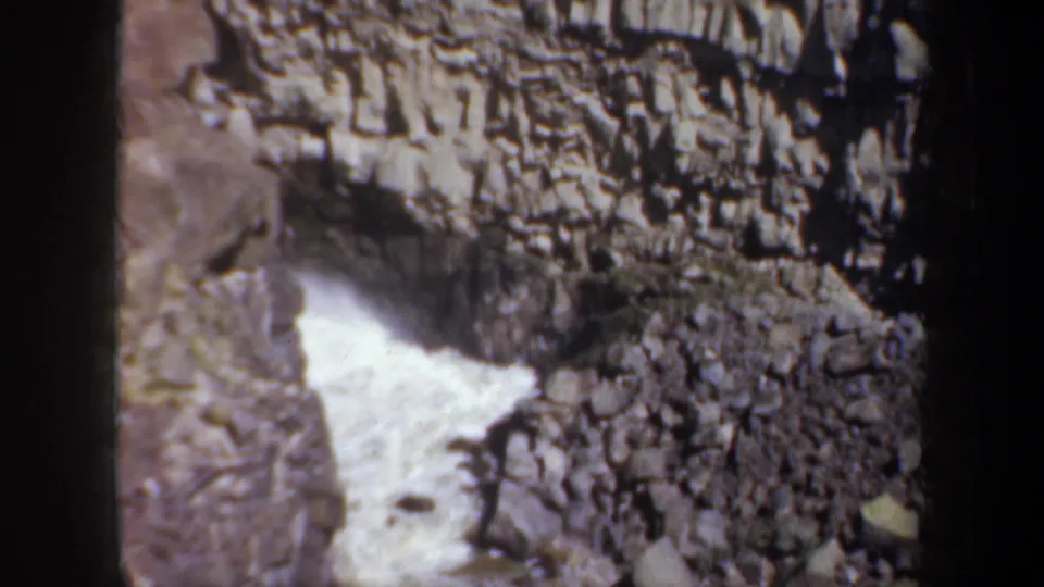1957 Oregon home-movie frame showing white water surging through a narrow rocky canyon beneath layered cliffs.