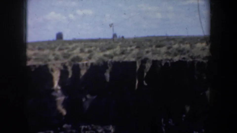 Wide 1957 Oregon home-movie view of a canyon-like rock formation under pale sky, with shadowed cliff faces below the rim.