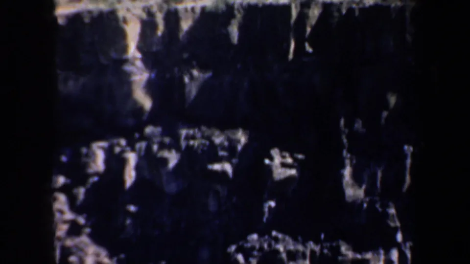Shadowed 8mm frame of jagged canyon rock with bright patches of moving water or reflected light near the lower edge.