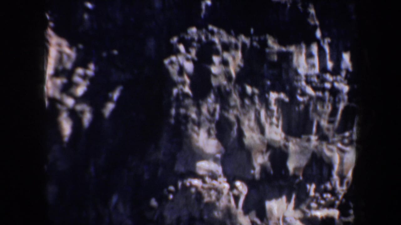 Shadowed rocky canyon wall in 1957 Portland-area 8mm footage, with jagged ledges and dark crevices filling the frame.