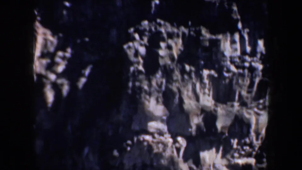 Shadowed rocky canyon wall in 1957 Portland-area 8mm footage, with jagged ledges and dark crevices filling the frame.