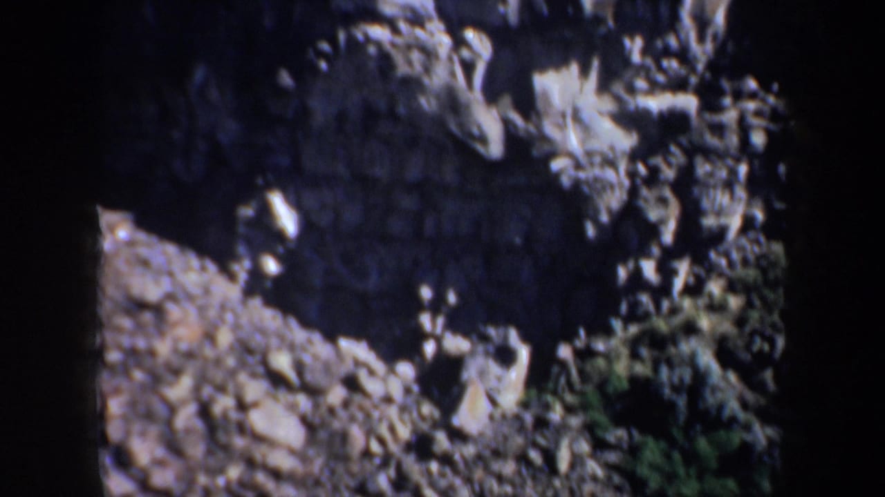 Steep rocky slope beside a darker canyon wall, with loose stones and sparse greenery.