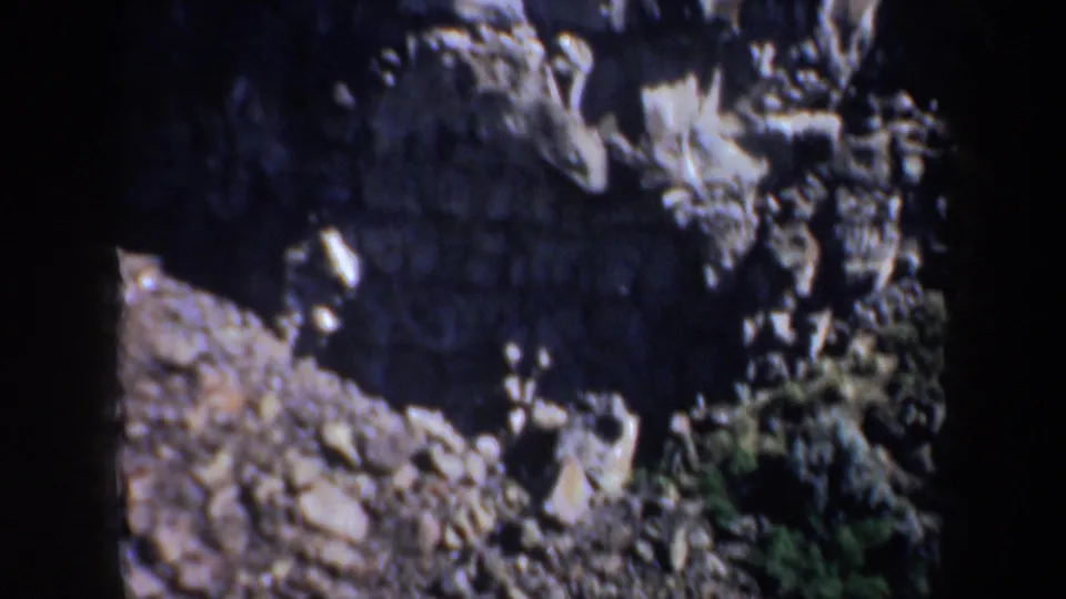 Steep rock and gravel slope in the Portland, Oregon 1957 home-movie clip, bordered by darker canyon walls and small vegetation patches.