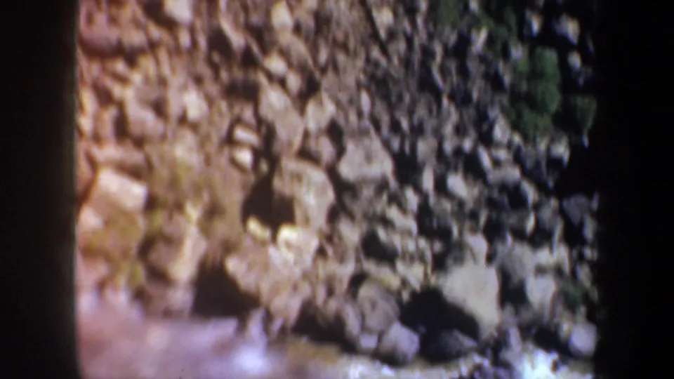 Soft 8mm frame of rocky canyon ground near Portland, Oregon, showing boulders, loose gravel, and a small patch of vegetation.