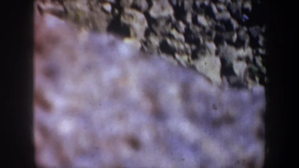 Final soft-focus 1957 Portland-area canyon frame, with a rocky slope in the foreground and darker stone surfaces beyond.