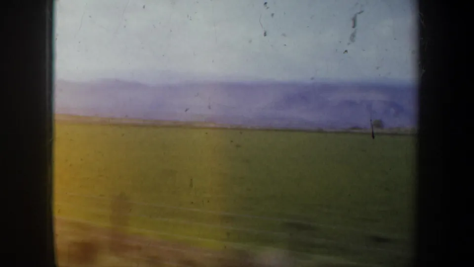 Wide 8mm view from the Portland, Oregon-associated footage showing green fields, distant purple hills, and a pale sky.