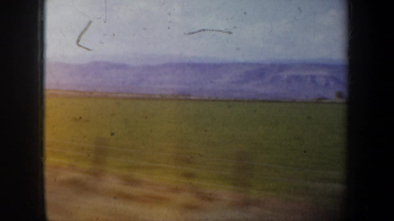 Open arid field and distant mountains seen through dark vehicle-window edges.