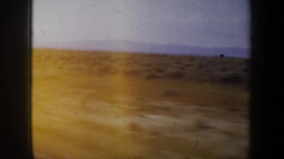 8mm home-movie frame showing a golden-brown hillside and distant blue-purple mountains under a pale sky.