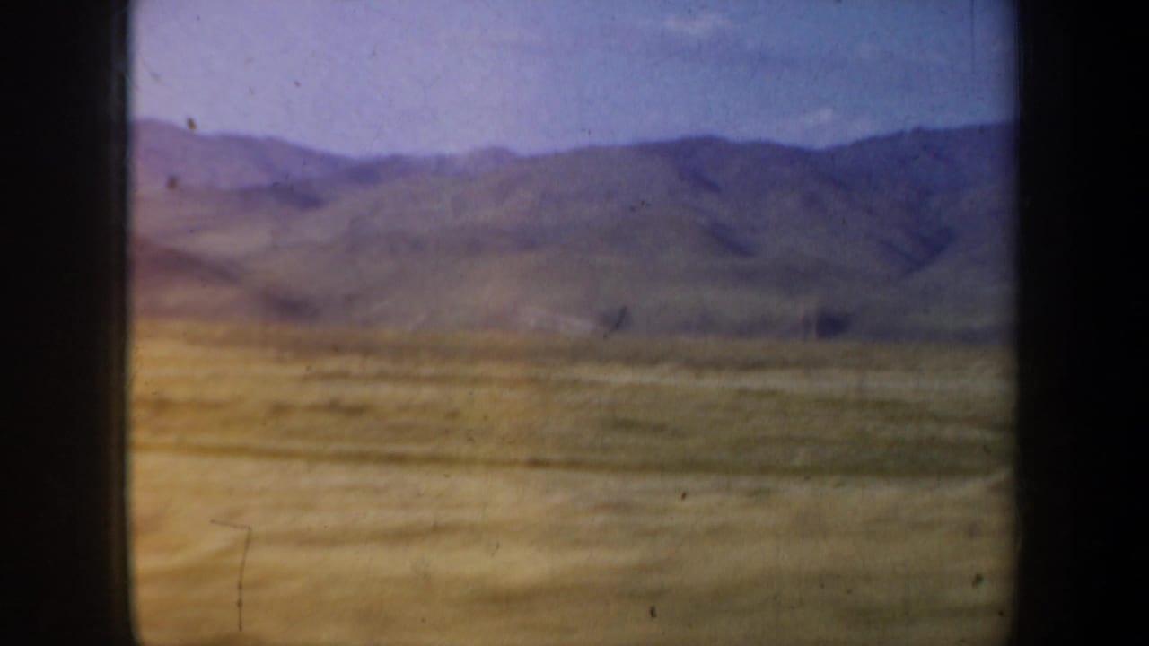 Distant mountains and dry open land seen through a dark vehicle window frame.