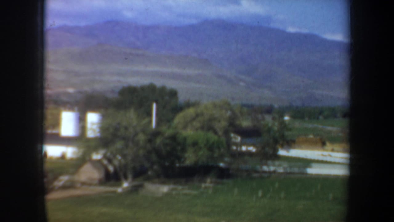 Green pasture and white farm buildings below distant hills and mountains.