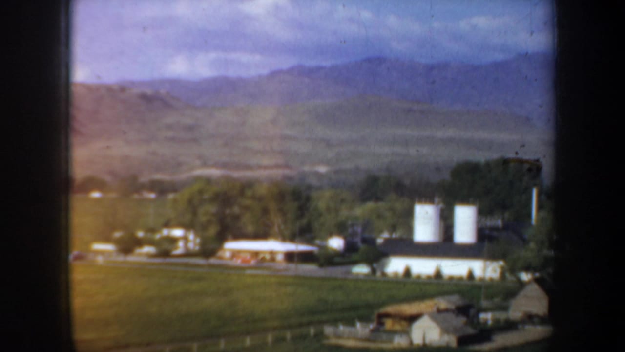 White silos and farm buildings across green fields with hills behind.