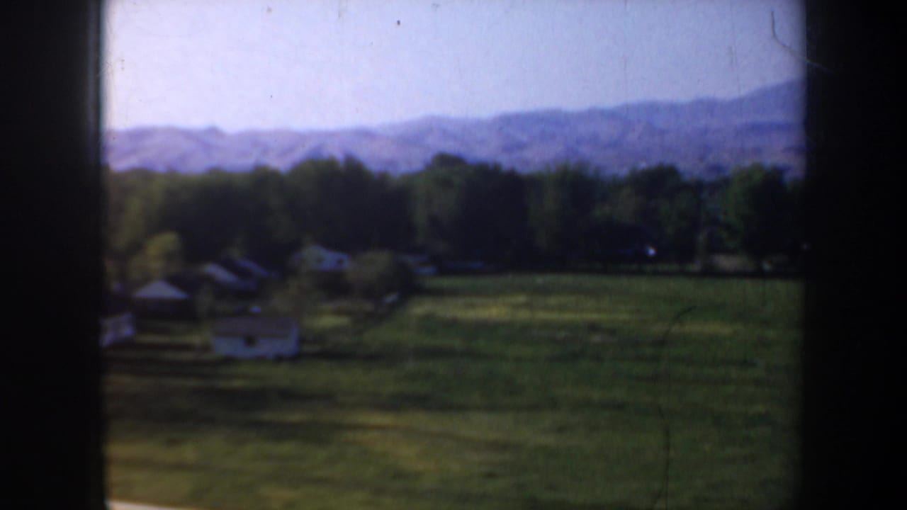 1957 Portland, Oregon area home-movie view of a green field, small houses, trees, and distant hills from a moving vehicle.