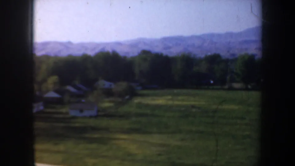1957 Portland, Oregon area home-movie view of a green field, small houses, trees, and distant hills from a moving vehicle.
