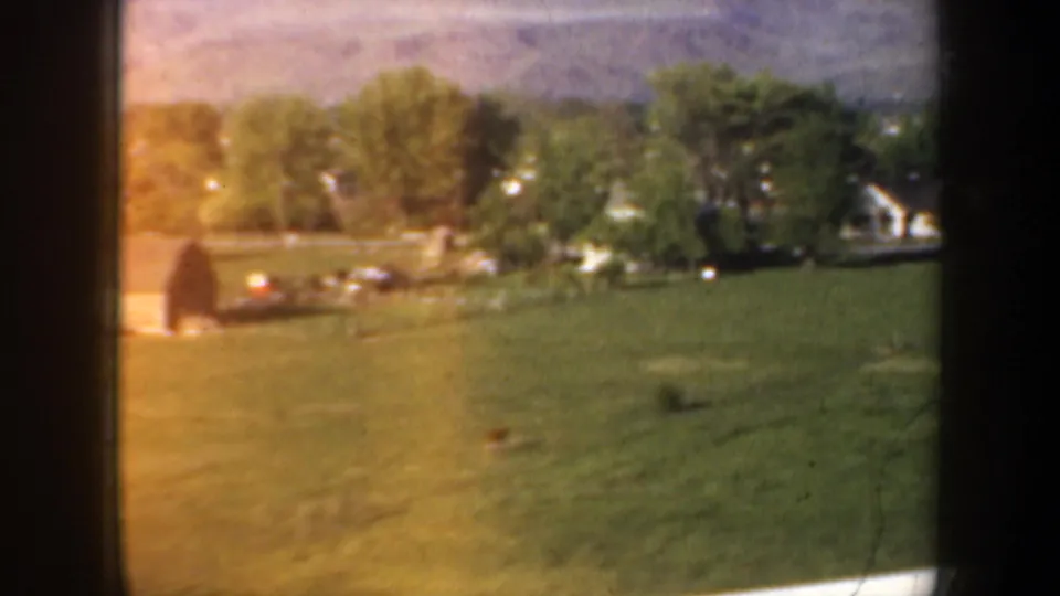 1957 Portland-area home-movie view of a green pasture, trees, and small light buildings through a vehicle window.