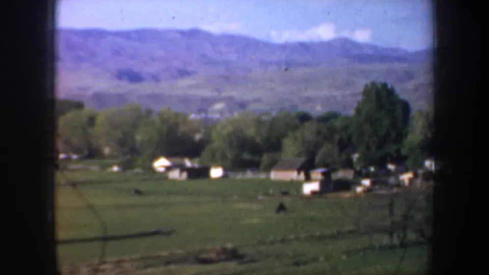 Open green field near Portland with small structures, trees, and distant hills, filmed from a moving vehicle in 1957.